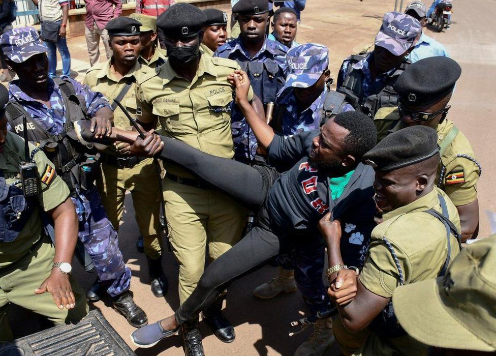 A man being lifted up and struggling against a group of officers who are man handling him.