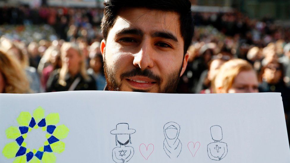 A man holds up a sign featuring symbols of different religions during a memorial ceremony at Sergels Torg plaza in Stockholm, Sweden on 9 April 2017