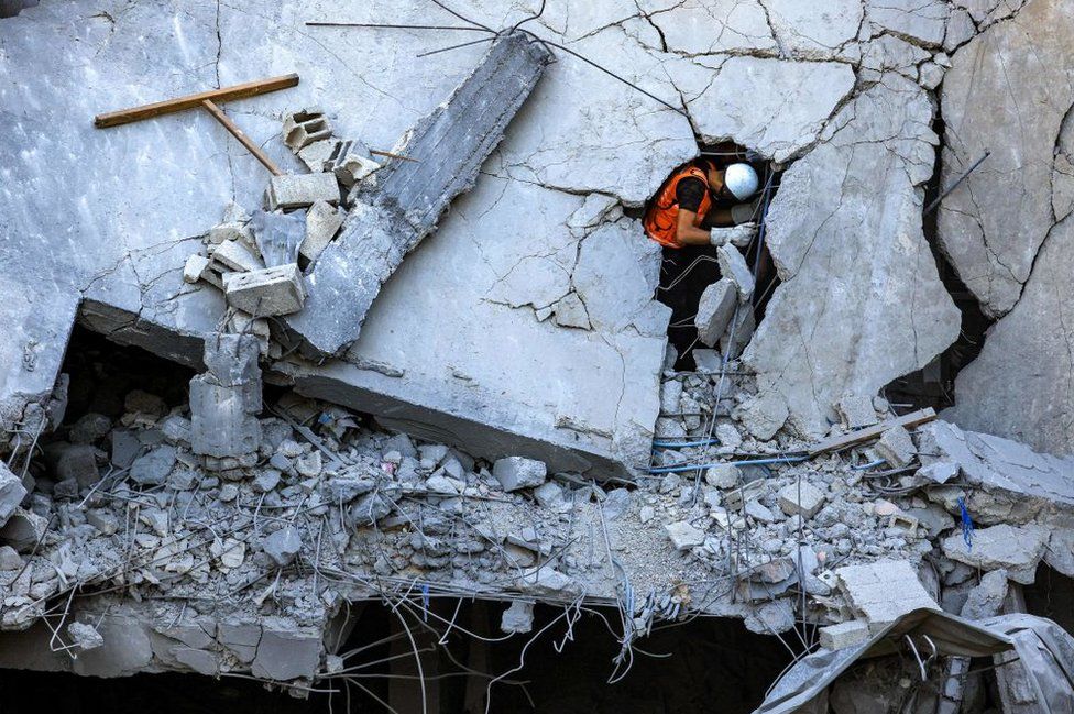 A Palestinian civil defence member stands through a crack in a collapsed building hit by Israeli bombardment while searching for victims and survivors, in Khan Younis in the southern Gaza Strip on October 19, 2023.