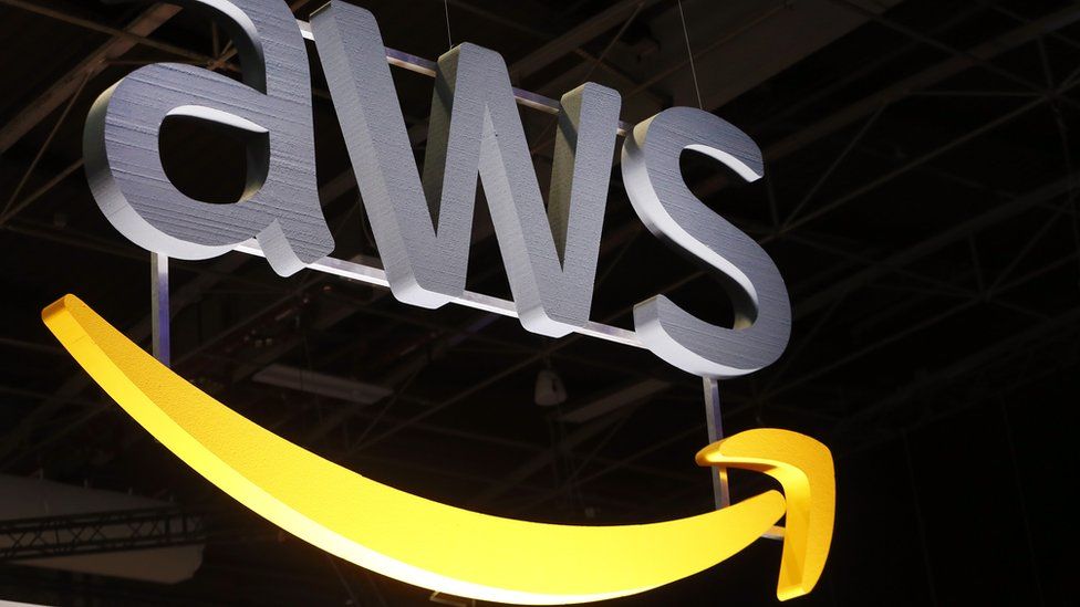 The AWS logo hangs suspended from a ceiling, lit dramatically from below