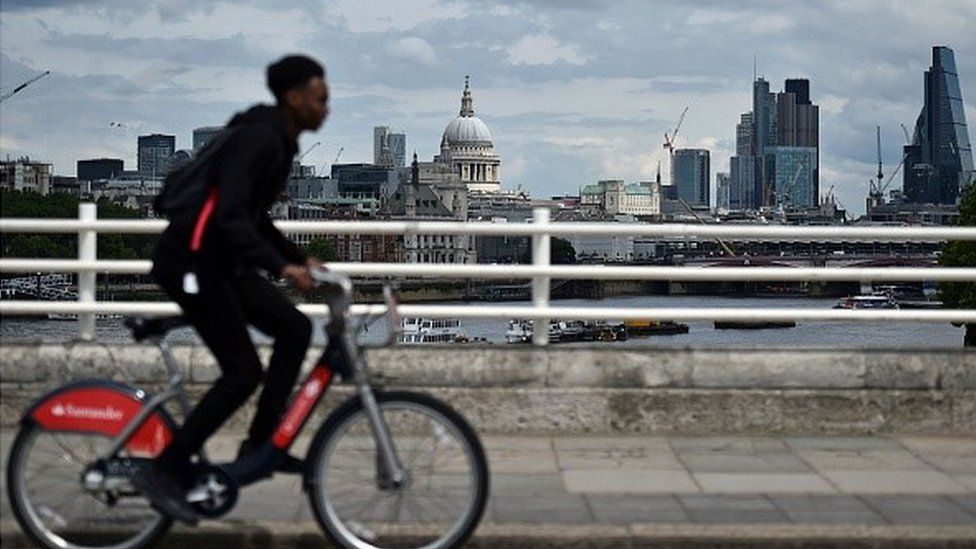 A Man rides a boris bike over Westminster bridge