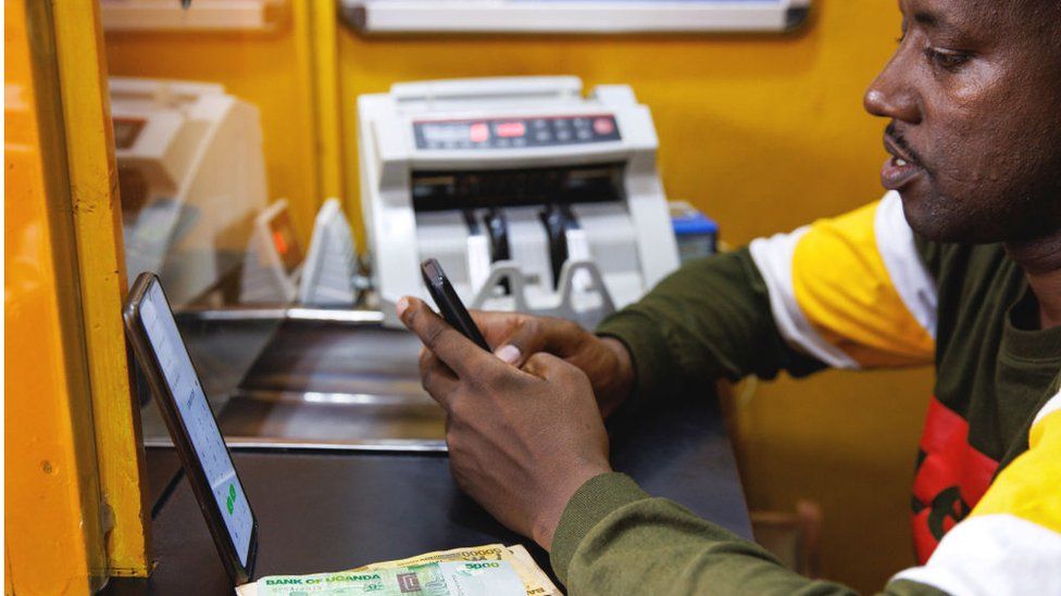 An agent carries out a mobile money transfer transaction with a customer inside a kiosk in Kampala, Uganda, on Wednesday, Aug. 16, 2023.