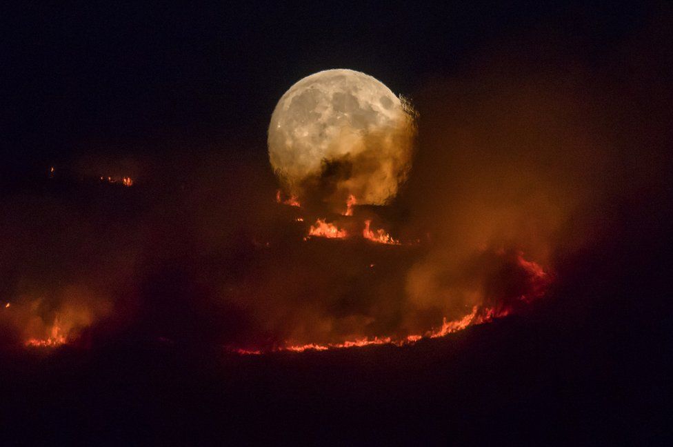 The full moon rises behind burning moorland