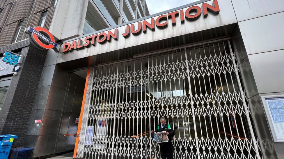 A man stands looking at a newspaper outside Dalston Junction Overground station, closed because of strike action