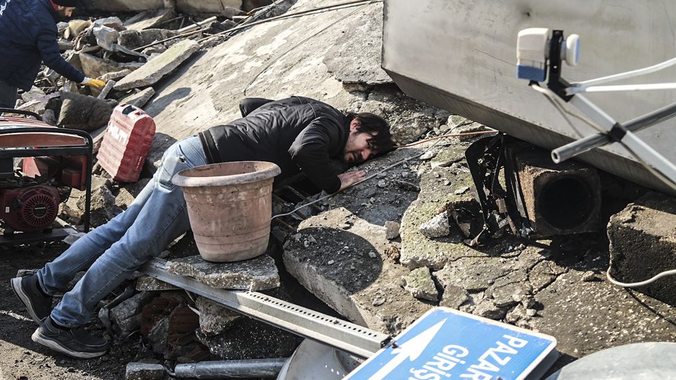 A man puts his ear to the rubble searching for the noise of any trapped person