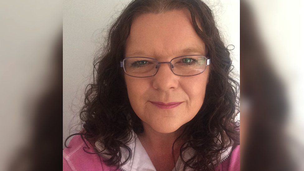 Julia Sealey. She is wearing glasses and a pink and white shirt. She has dark curly hair. She is smiling at the camera.