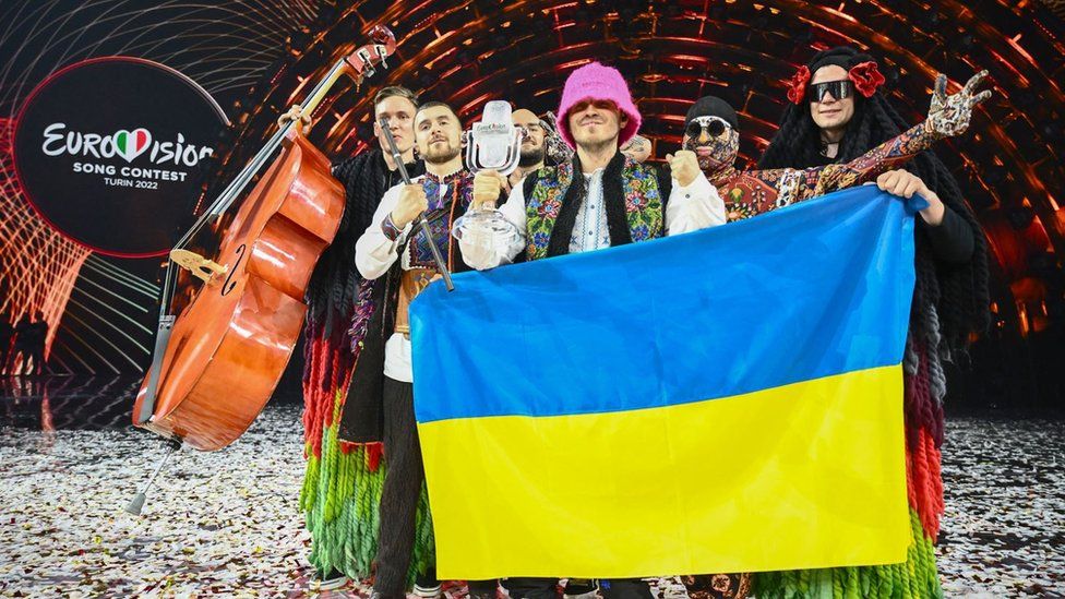 Участники группы "Kalush Orchestra" позируют на сцене с кубком победителя и флагами Украины после победы от имени Украины на конкурсе "Евровидение-2022"