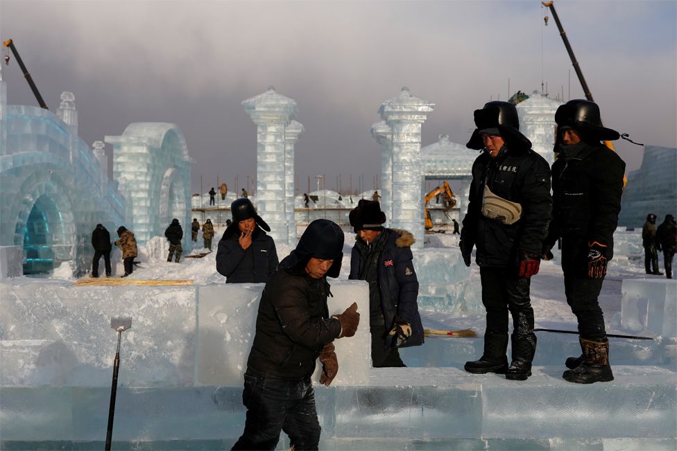 Workers smoke while constructing ice structures at the site of the Harbin International Ice and Snow Festival