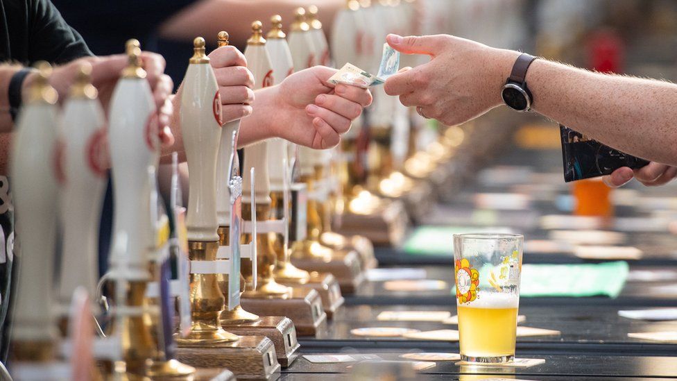 Row of beer pumps in a bar with bar staff taking money from customer