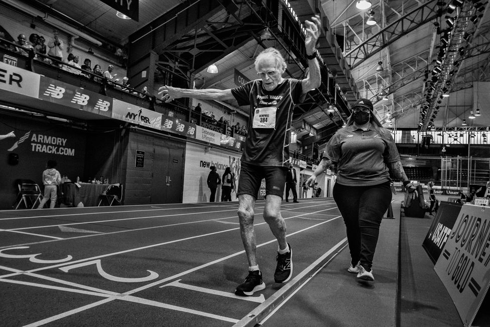 Dixon Hemphill, 97, of Potomac Valley Track Club, crosses the finish line in the M95 (Men 95-99) 200 meter dash, accompanied by a young woman for safety.