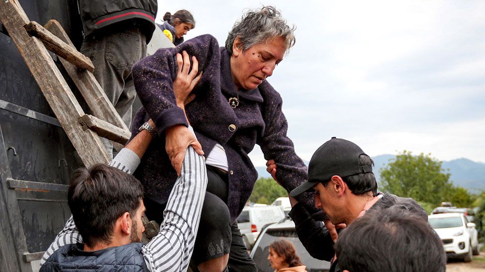 A refugee woman from Nagorno-Karabakh region is helped to get out of the back of a truck upon arrival in the border village of Kornidzor, Armenia, on 26 September 2023