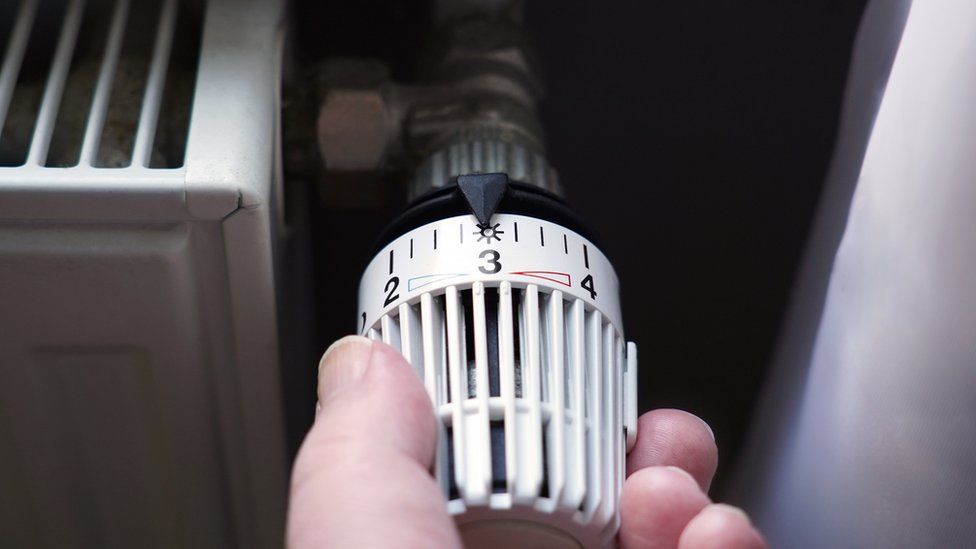 hand turning down thermostat on radiator to save energy due to heating cost price hike