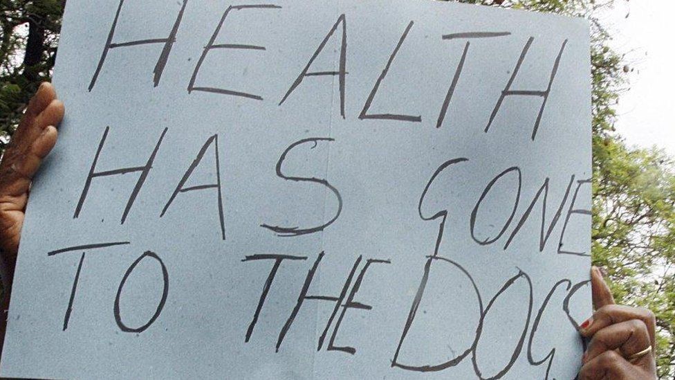 A protester holds up a poster that reads 'Health has gone to the dogs'