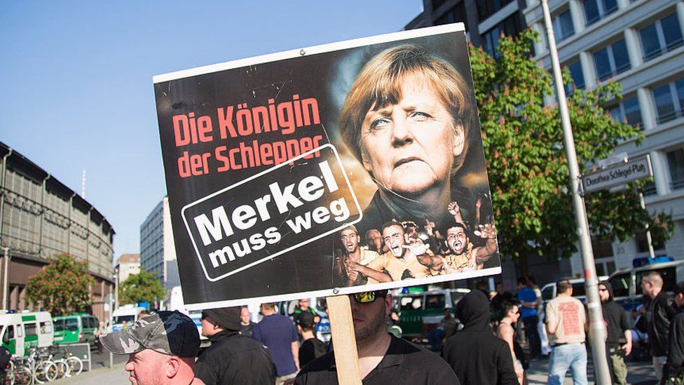 A protestor holds a banner which says "Merkel must go"