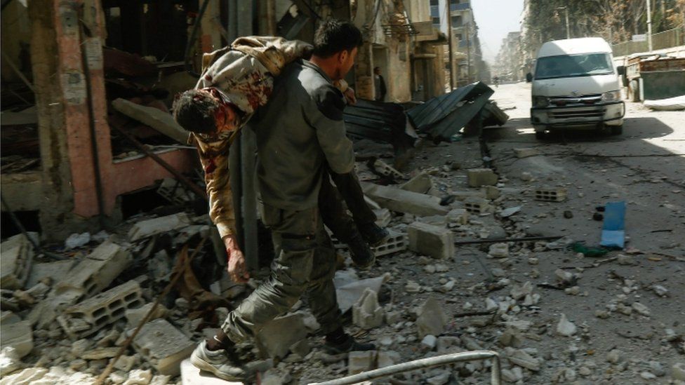 A member of the White Helmets carries a wounded man over his shoulder through the rubble of a destroyed building