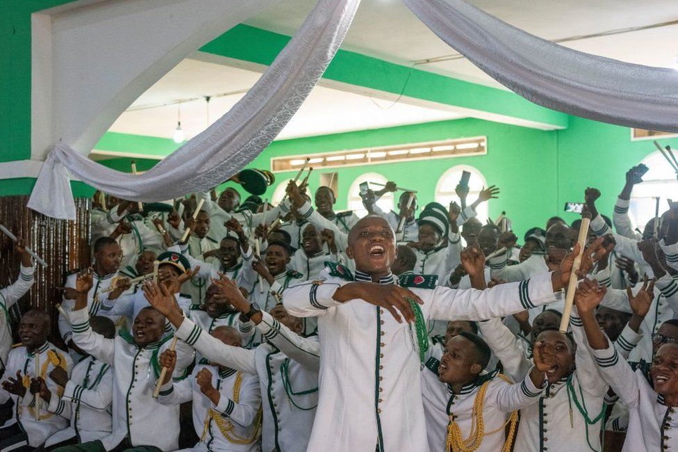 People in matching marching band uniforms sing and celebrate at Congo's International Kimbanguist Church.