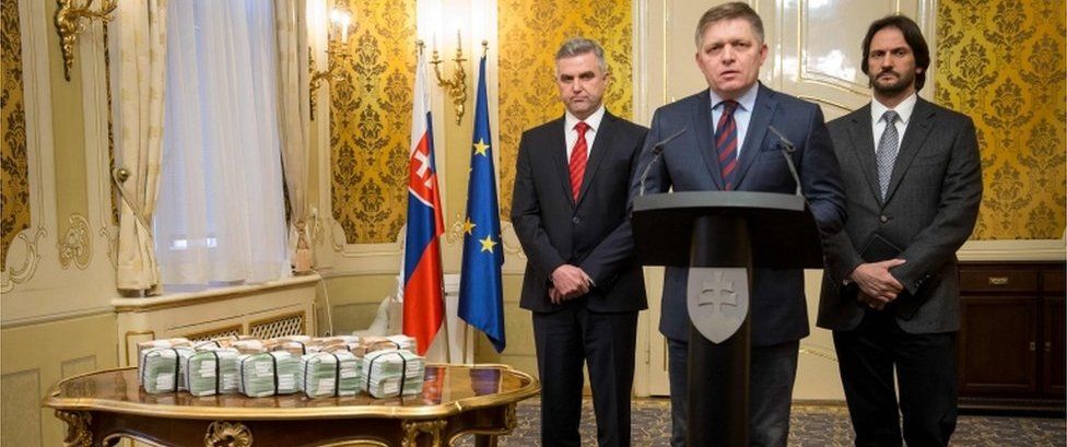 Slovak Prime Minister Robert Fico (C) is flanked by Slovak Police President Tibor Gaspar (L) and Slovak Interior Minister Robert Kalinak (R) next to bundles of euro banknotes