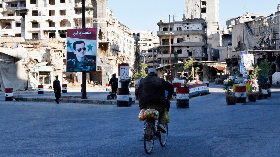 A Syrian rides a bicycle towards a check point amid the ruins of buildings in the old city of Homs (7 December 2015)