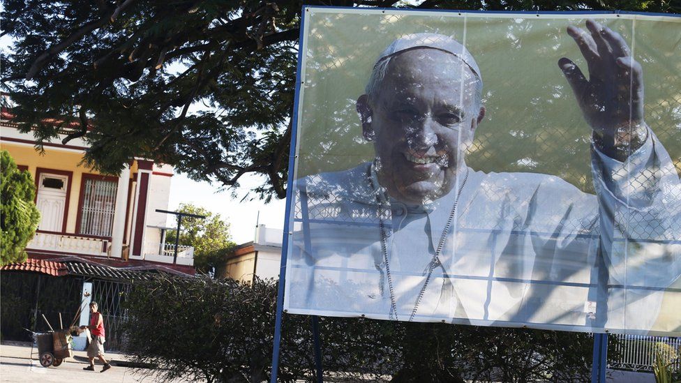 A street sweeper walks near a sign with a photograph of Pope Francis in Havana