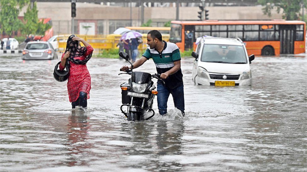 Пассажиры едут по заболоченной местности среди проливных дождей возле Верховного суда Индии, 9 июля 2023 года, Нью-Дели, Индия.