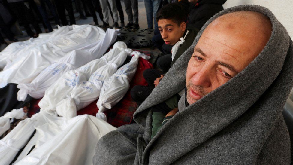 Mourners sit next to the bodies of Palestinians killed in Israeli strikes, at a hospital in Rafah, in the southern Gaza Strip (19 December 2023)