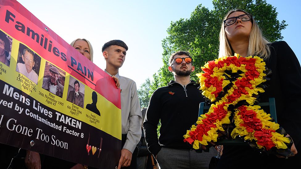 Families affected by the infected blood scandal hold a banner showing images of deceased relatives as they wait to enter the Methodist Central Hall to hear the findings of the six-year inquiry on May 20, 2024 in London, England