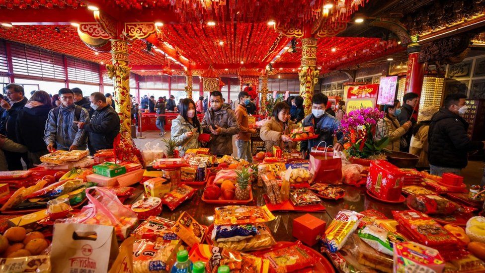 Dozens of people placing food on a table in a temple for Lunar New Year