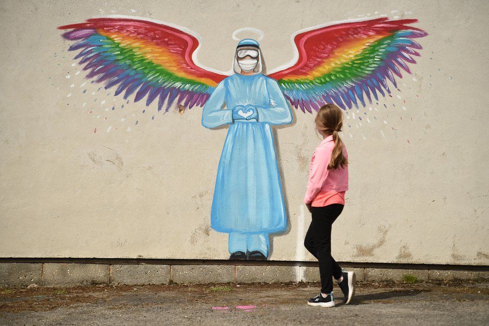 A girl walks past a mural of a doctor with rainbow angel wings