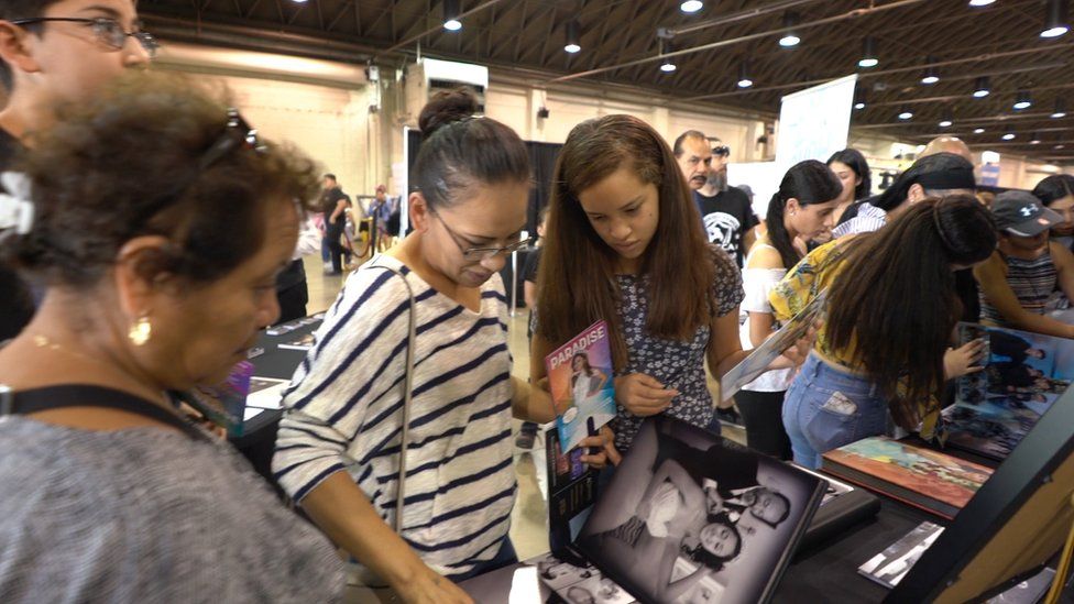 Asistentes a la feria de la revista Quinceañera miran catálogos de servicios de fotografía para el evento