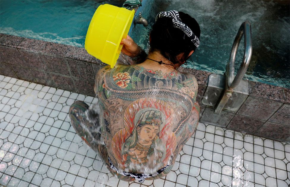 A man with body tattoos pours water over his back
