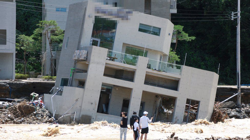 People stand in front of a collapsed building on a beach in Pohang