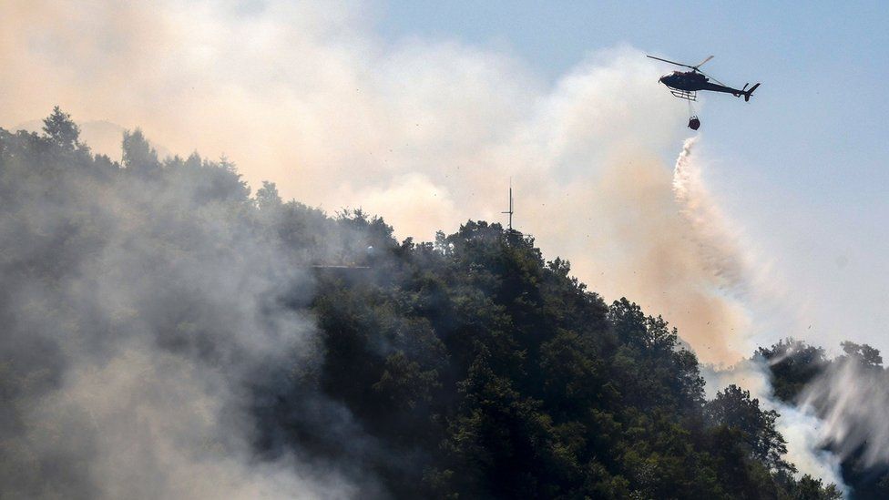 A helicopter drops water as firefighters work to extinguish a wild fire in Mount Dajti, east of capital Tirana, 4 August 2017