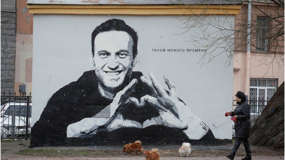 A woman walks her dogs in front of a graffiti depicting jailed Russian opposition politician Alexei Navalny in Saint Petersburg, Russia April 28, 2021