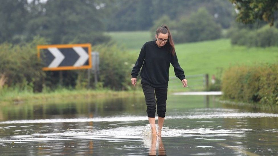 A woman makes her way along the flooded Bonis Hall Lane, Prestbury, Cheshire