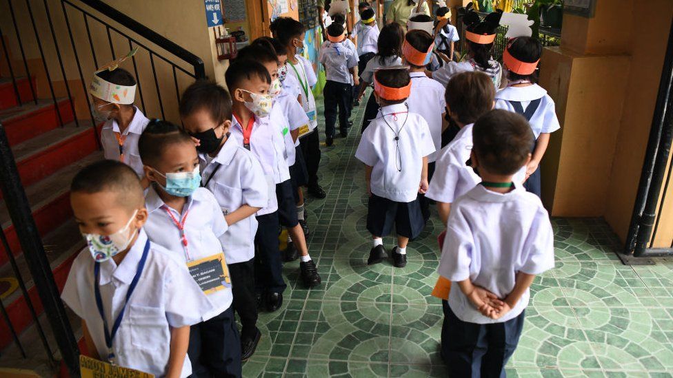Учителя смотрят, как их ученики идут по коридору после короткого перерыва в начале занятий в школе в Кесон-Сити