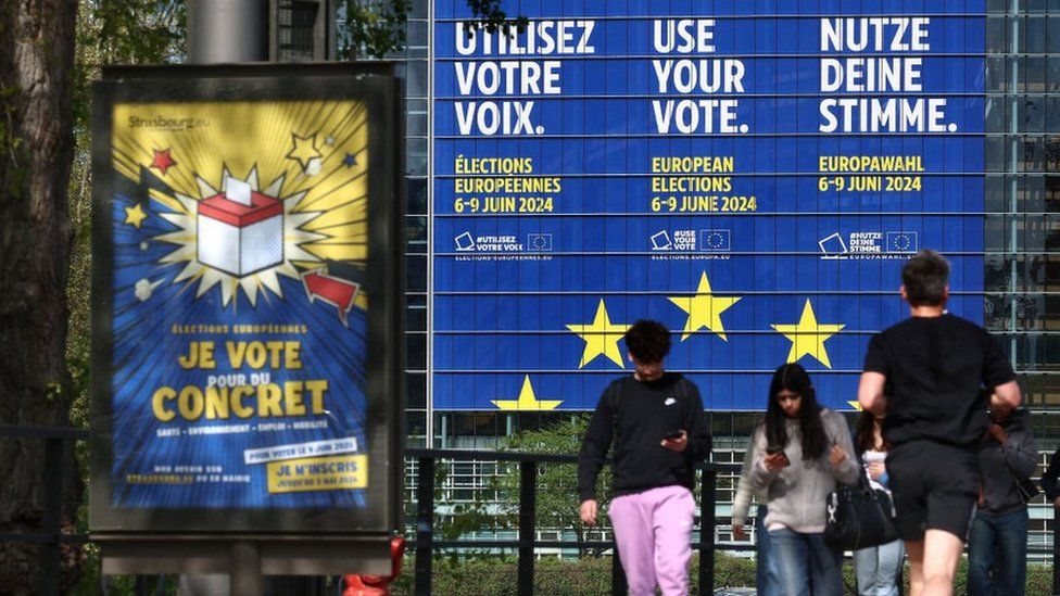 Pedestrians walk pass a giant poster announcing the upcoming European elections, stuck on the facade of the European Parliament building, in Strasbourg, eastern France, on April 10, 2024. The European Parliament elections are planned to be held from June 6 to 9, 2024