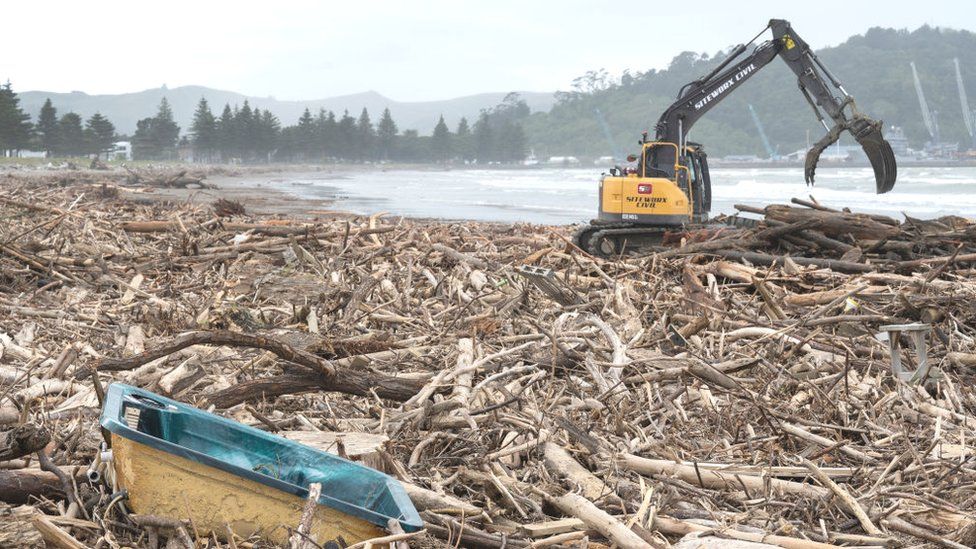 Heavy equipment clear debris by the beach after Cyclone Gabrielle in New Zealand.