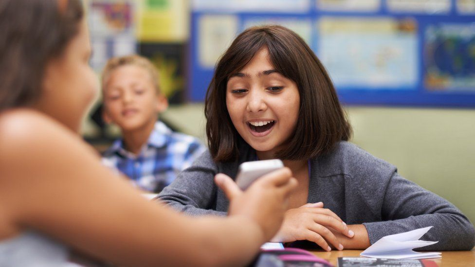 Девочка смотрит в экран телефона в школе