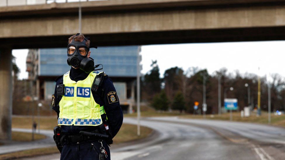 Police officer wearing gas mask outside Sweden security service HQ on Friday