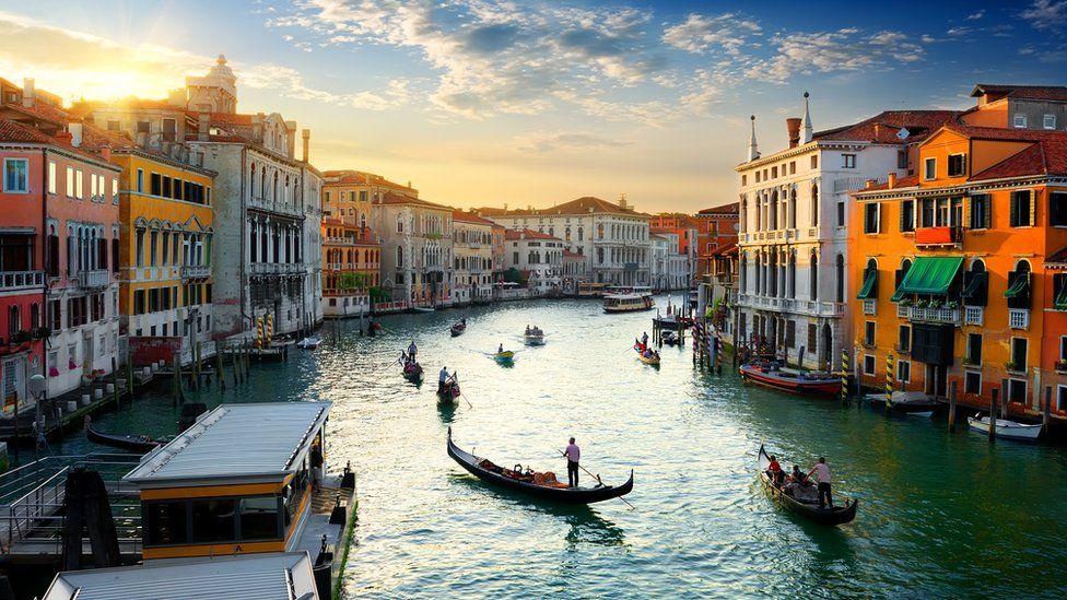 A few boats slip through the broad expanse of the Venice Grand canal in golden late evening light