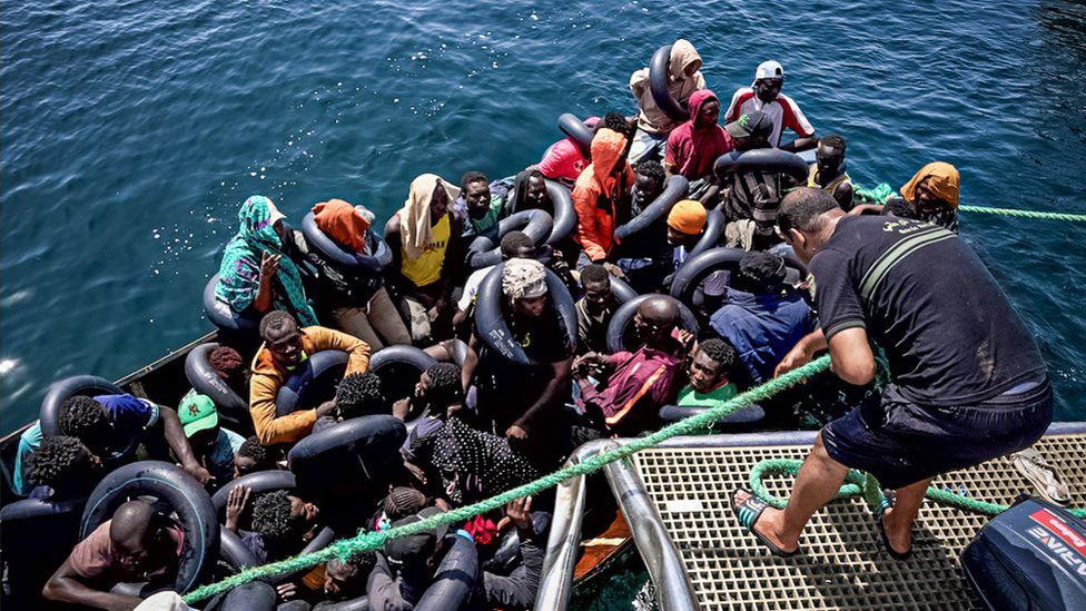 Судно с нелегальными мигрантами привязывается к патрульному катеру тунисской береговой охраны, прежде чем его пассажиров попросят сойти