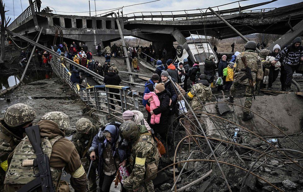 People cross a destroyed bridge as they evacuate the city of Irpin, northwest of Kyiv, during heavy shelling and bombing on March 5, 2022, 10 days after Russia launched a military invasion on Ukraine