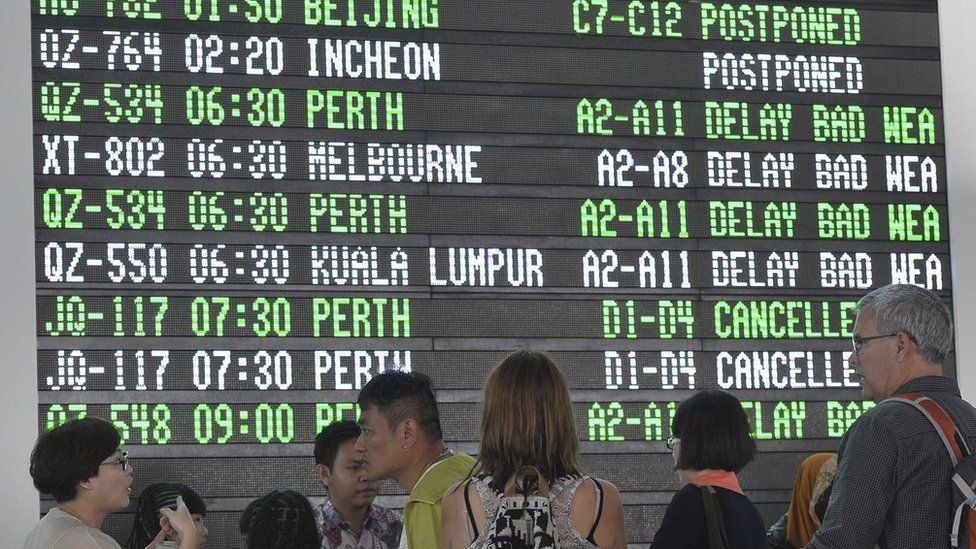 Passengers stand near the Departure Board in the international terminal at Ngurah Rai Airport on the Indonesian resort island of Bali July 10, 2015