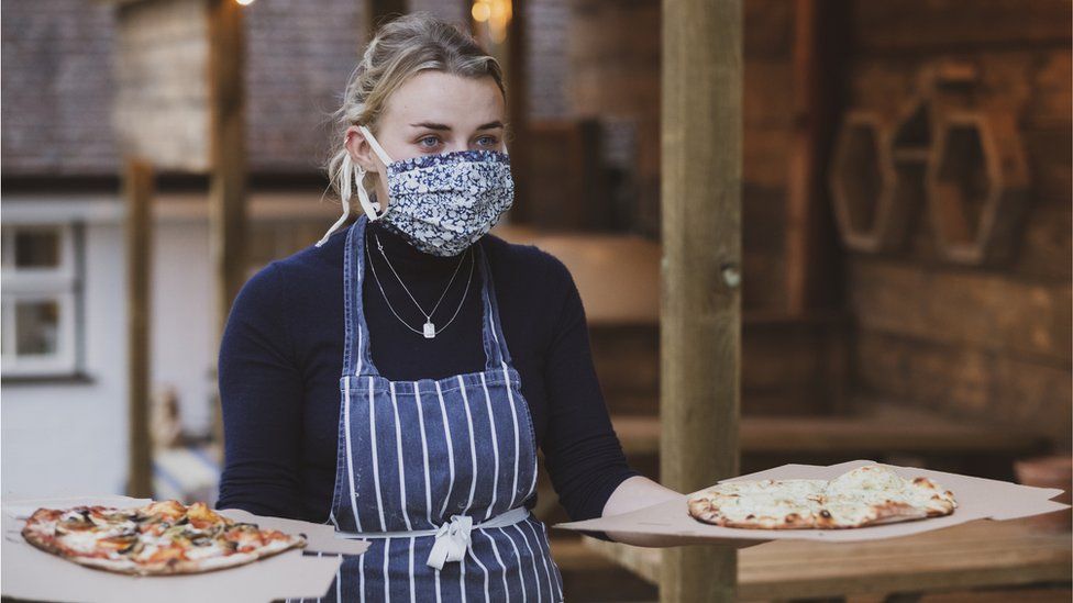 Waitress carries pizzas while wearing a face mask