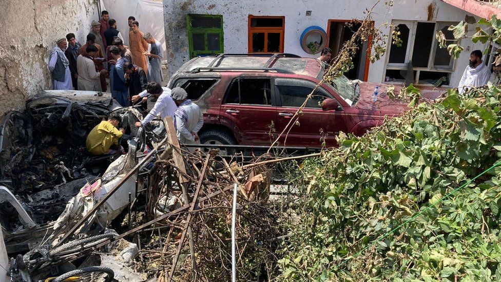 A photograph showing the destroyed car and damage around it