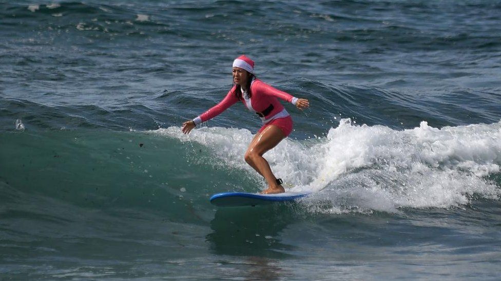 A woman wearing a Santa hat and bathing suit goes surfing on Christmas Day at Bondi Beach in Sydney, Australia, 25 December 2023.
