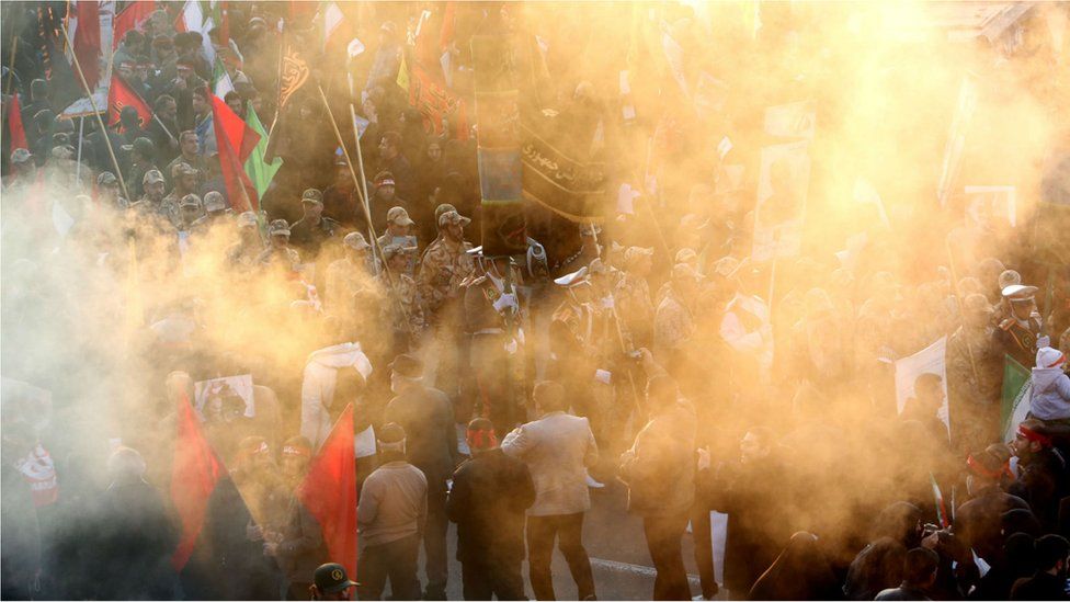 An Iranian military parade is seen behind a smoke screen from burning incense as crowds gather to pay homage to military commander Qasem Soleimani, Iraqi paramilitary chief Abu Mahdi al-Muhandis and other victims of a US drone attack, in the capital Tehran on 6 January, 2020
