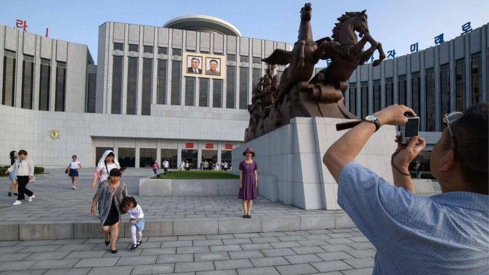Tourists pose for photos in front of The Children's Palace in Pyongyang