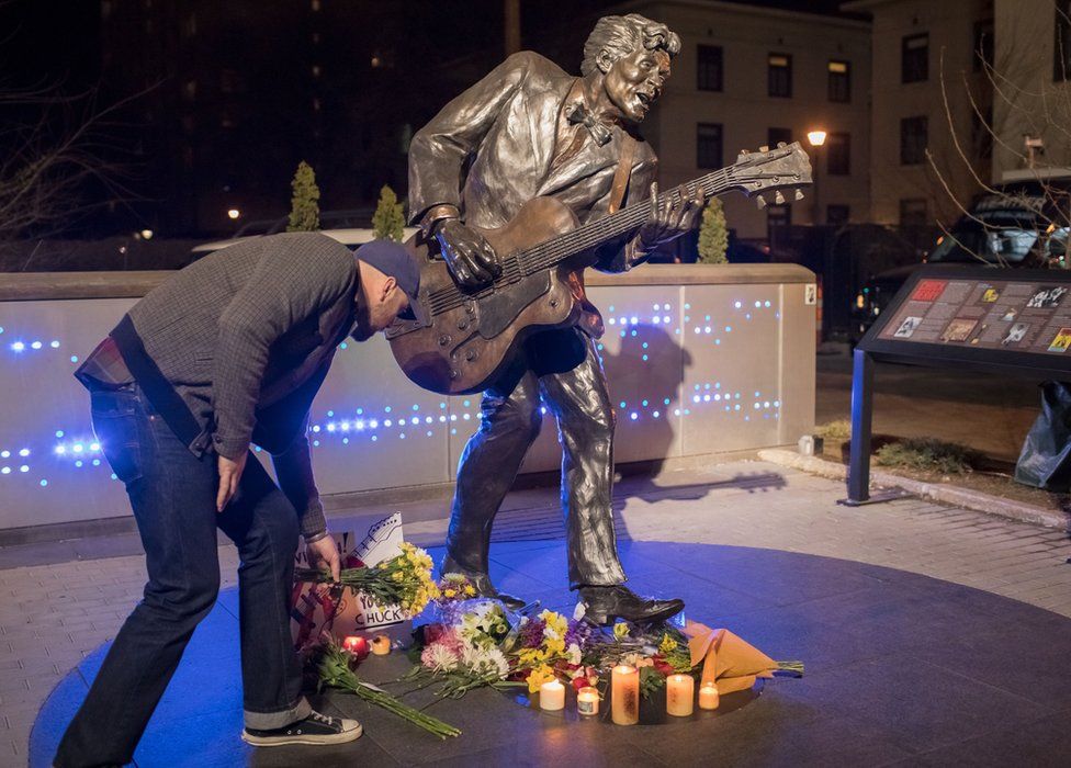 A man places flowers below a statue of singer and musician Chuck Berry in University City, Missouri, on March 18, 2017