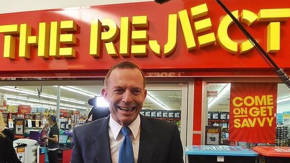 Tony Abbott outside a shop named 'reject'